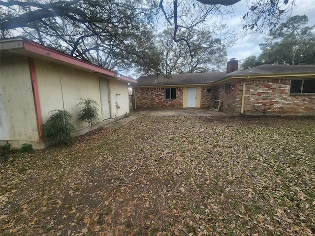 back of house with brick siding, a chimney, and a patio area