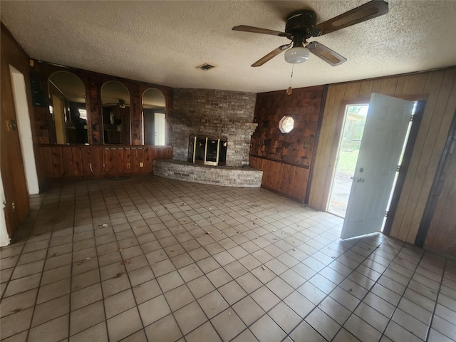 unfurnished living room featuring visible vents, wood walls, a fireplace, and a ceiling fan