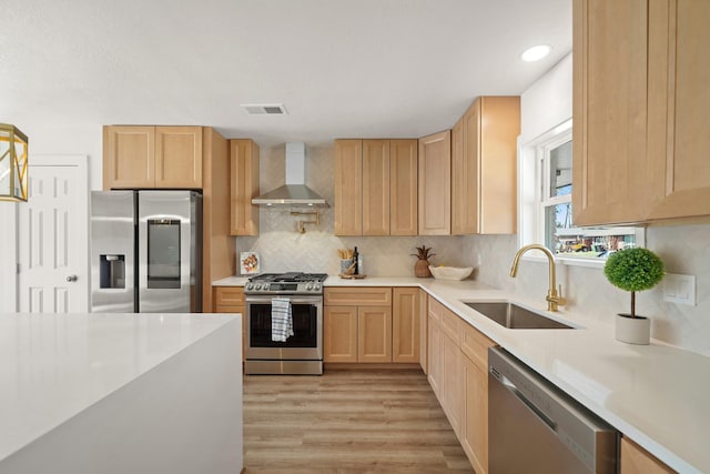 kitchen featuring visible vents, light brown cabinetry, a sink, appliances with stainless steel finishes, and wall chimney range hood