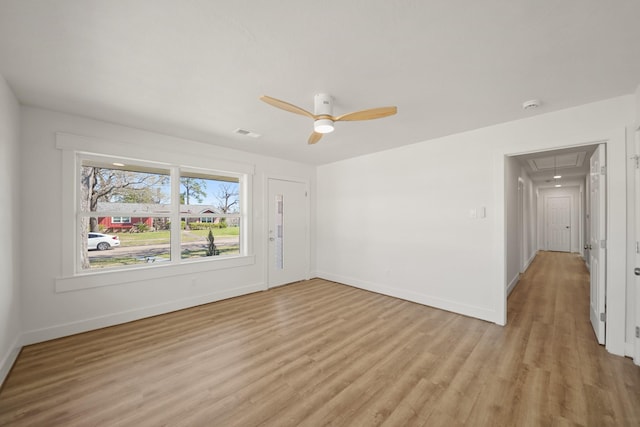 empty room with ceiling fan, baseboards, attic access, and light wood-style flooring