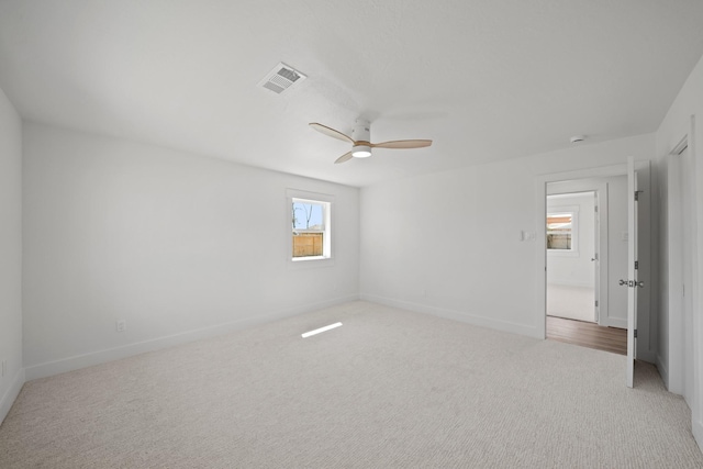 spare room with ceiling fan, baseboards, visible vents, and light carpet