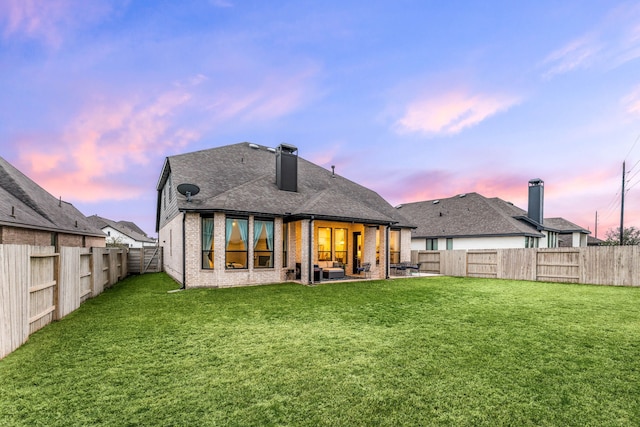 back of property with brick siding, a fenced backyard, a chimney, a patio area, and a lawn