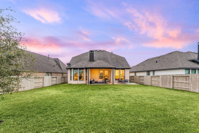 back of house at dusk with a patio, a lawn, a fenced backyard, and a shingled roof