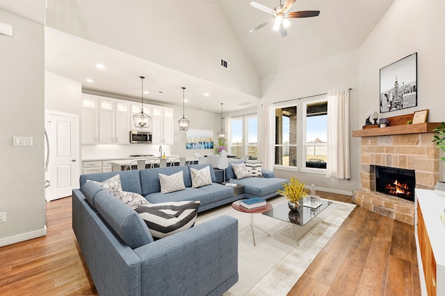 living area with light wood finished floors, visible vents, baseboards, a fireplace, and high vaulted ceiling