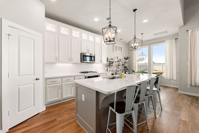 kitchen featuring stainless steel microwave, backsplash, visible vents, and a sink