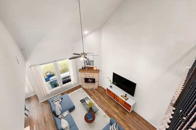 living room with a stone fireplace, a ceiling fan, wood finished floors, and high vaulted ceiling