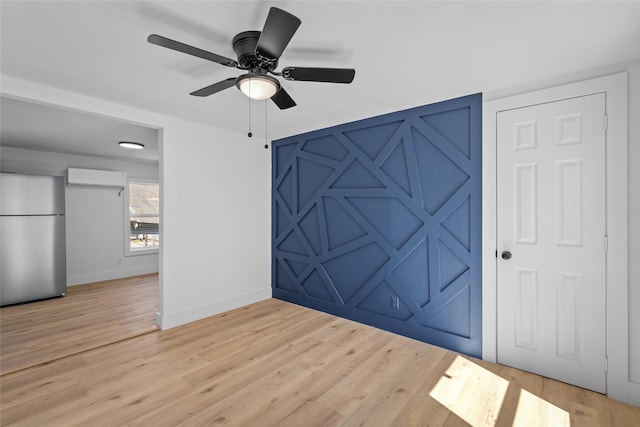 interior space with an AC wall unit, a ceiling fan, freestanding refrigerator, light wood finished floors, and baseboards