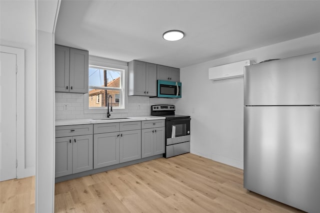 kitchen featuring an AC wall unit, gray cabinetry, electric stove, a sink, and freestanding refrigerator