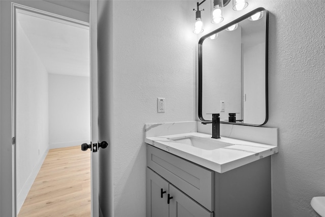 bathroom with vanity, wood finished floors, baseboards, and a textured wall