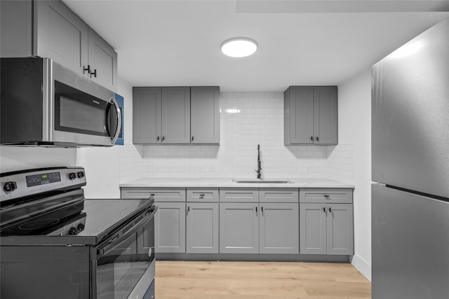 kitchen with decorative backsplash, gray cabinets, light wood-style floors, stainless steel appliances, and a sink