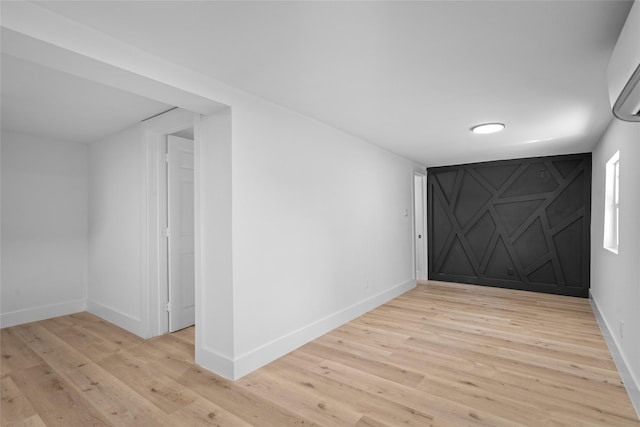 unfurnished room featuring an AC wall unit, light wood-type flooring, and baseboards