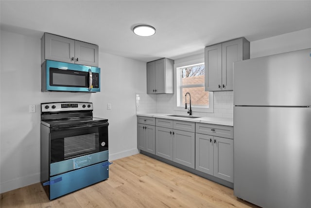 kitchen with gray cabinetry, a sink, light wood-style floors, appliances with stainless steel finishes, and tasteful backsplash