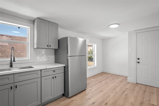 kitchen with gray cabinets, light wood-type flooring, freestanding refrigerator, and a sink