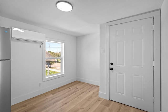 spare room featuring an AC wall unit, baseboards, and light wood-type flooring