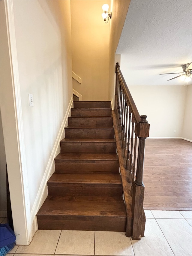 stairway featuring tile patterned floors, ceiling fan, a textured ceiling, and baseboards