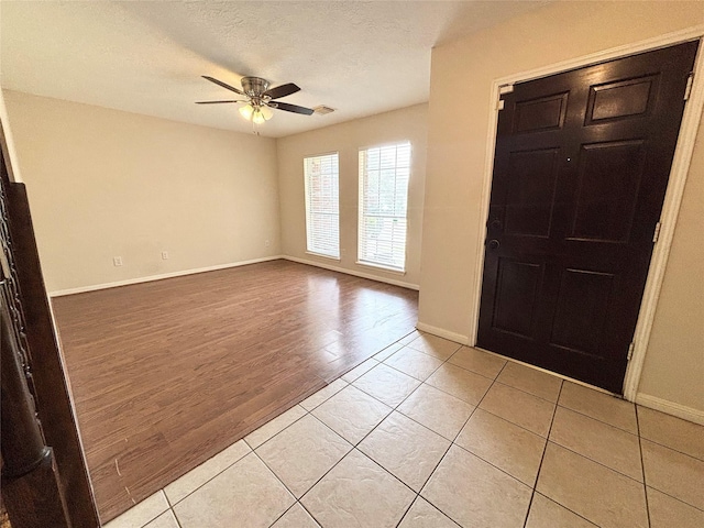 entrance foyer featuring a ceiling fan, visible vents, baseboards, light wood finished floors, and a textured ceiling