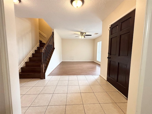 foyer featuring a ceiling fan, a textured ceiling, light tile patterned floors, baseboards, and stairs