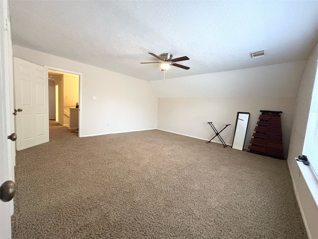 carpeted spare room with lofted ceiling, a ceiling fan, visible vents, and a textured ceiling