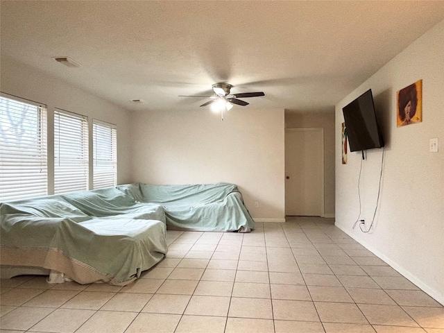 living area with visible vents, a textured ceiling, light tile patterned flooring, baseboards, and ceiling fan