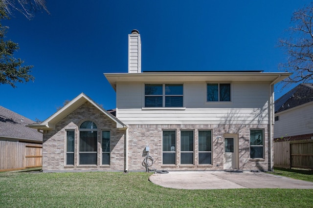 rear view of house featuring brick siding, fence, a yard, and a patio area