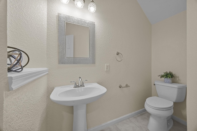 half bathroom featuring baseboards, toilet, tile patterned floors, a textured wall, and vaulted ceiling