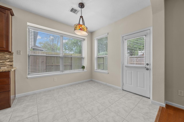 unfurnished dining area featuring baseboards, visible vents, light tile patterned floors, and plenty of natural light