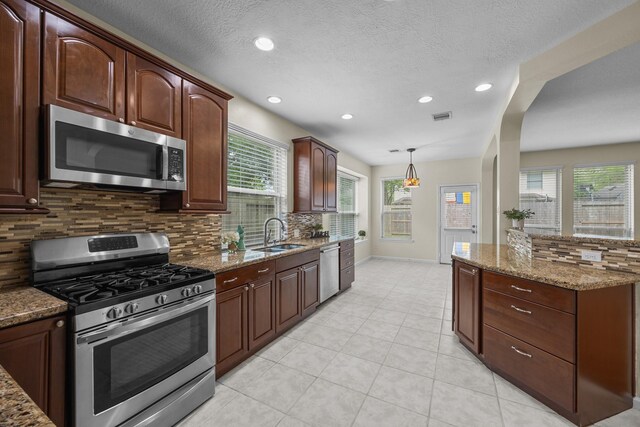 kitchen featuring visible vents, light stone countertops, stainless steel appliances, a sink, and backsplash