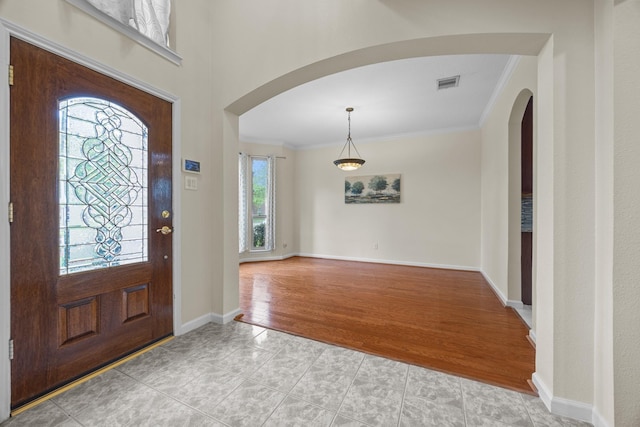 entryway featuring arched walkways, baseboards, visible vents, and crown molding