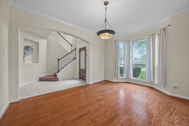 spare room featuring stairway, wood finished floors, baseboards, arched walkways, and ornamental molding