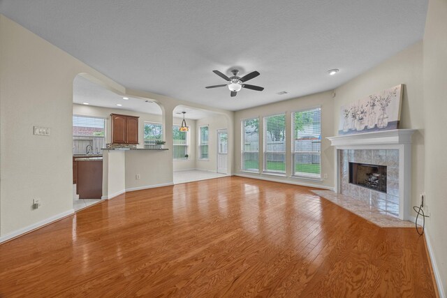 unfurnished living room featuring light wood-style flooring, baseboards, arched walkways, a tiled fireplace, and a ceiling fan