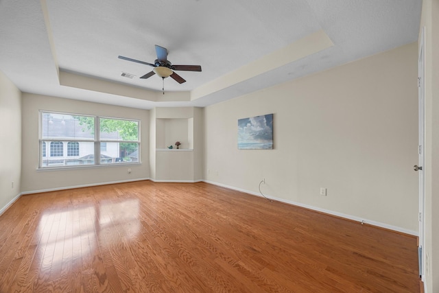 empty room with visible vents, baseboards, ceiling fan, wood finished floors, and a raised ceiling