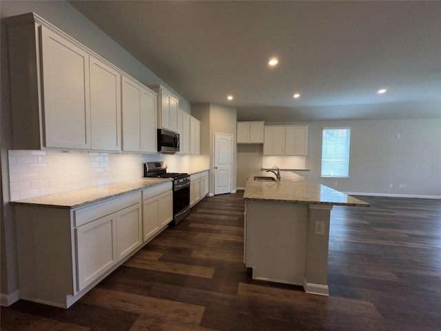 kitchen with light stone countertops, dark wood-style flooring, stainless steel appliances, white cabinets, and backsplash