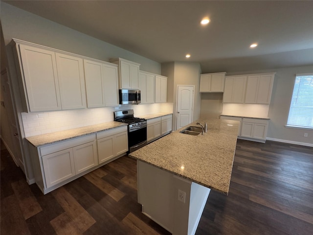 kitchen with a kitchen island with sink, a sink, tasteful backsplash, appliances with stainless steel finishes, and white cabinets