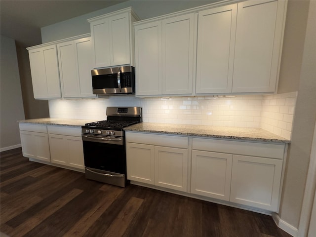 kitchen featuring dark wood-type flooring, light stone counters, stainless steel appliances, white cabinets, and decorative backsplash