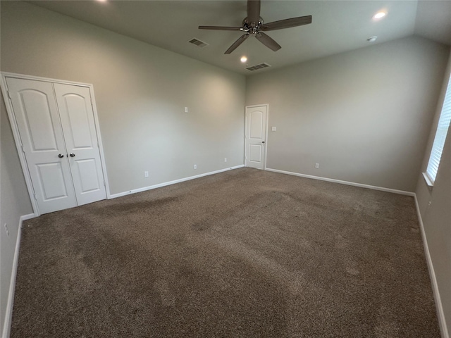 empty room featuring visible vents, lofted ceiling, and dark carpet