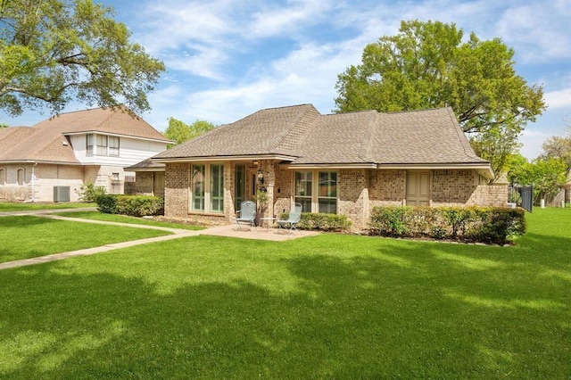 view of front of home with a patio, brick siding, a front lawn, and roof with shingles