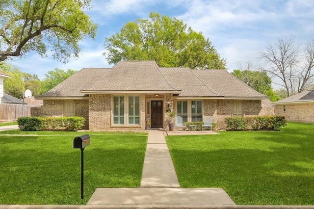 view of front of property with brick siding, fence, a front yard, and roof with shingles