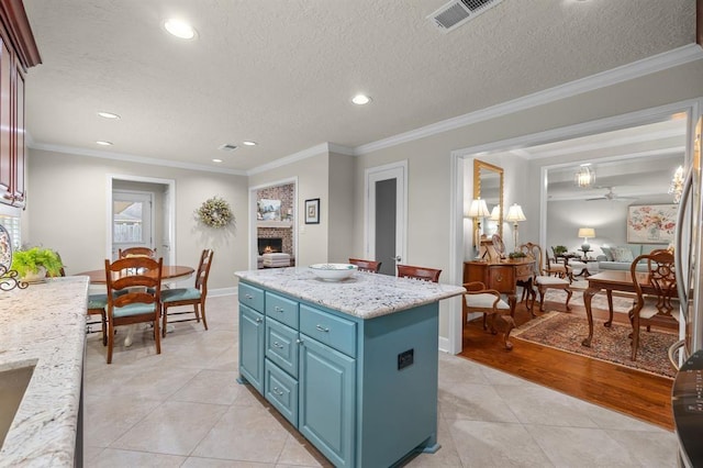 kitchen with visible vents, blue cabinetry, a lit fireplace, crown molding, and a center island