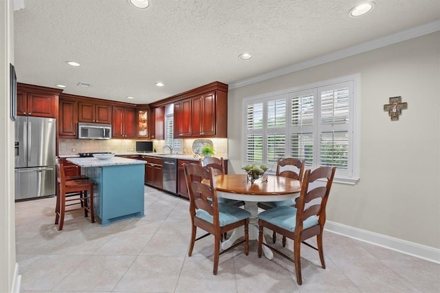 kitchen featuring backsplash, a kitchen island, baseboards, appliances with stainless steel finishes, and a sink