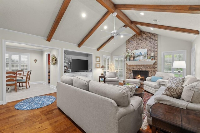 living area featuring a brick fireplace, ceiling fan, baseboards, lofted ceiling with beams, and wood finished floors