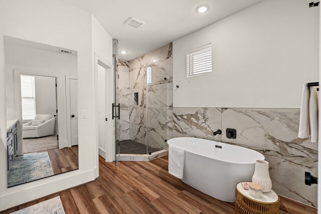 bathroom featuring a marble finish shower, a soaking tub, tile walls, and wood finished floors