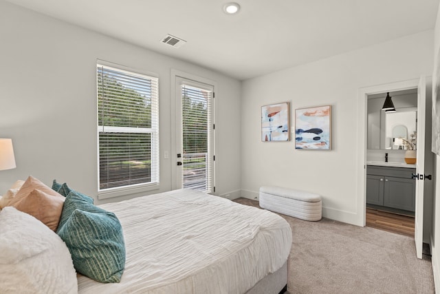 carpeted bedroom with visible vents, baseboards, ensuite bathroom, access to outside, and a sink