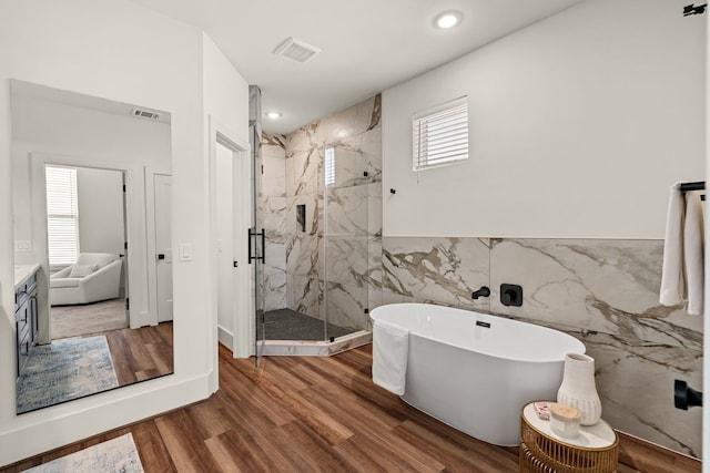 bathroom featuring visible vents, wood finished floors, a marble finish shower, tile walls, and a soaking tub