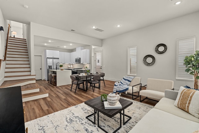 living area with stairway, wood finished floors, visible vents, baseboards, and recessed lighting