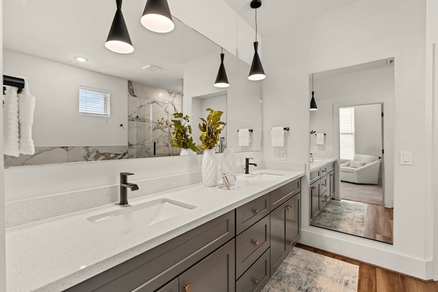 full bath with a sink, a marble finish shower, wood finished floors, and double vanity