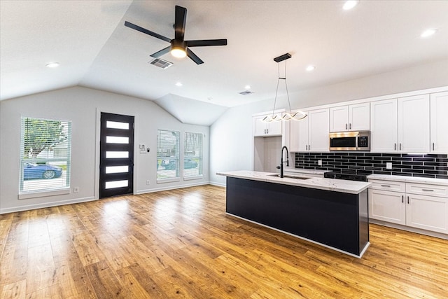 kitchen with a sink, stainless steel microwave, open floor plan, and decorative backsplash