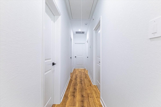 hallway featuring visible vents, attic access, a textured wall, and wood finished floors