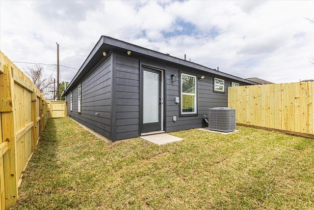 rear view of property featuring a lawn, a fenced backyard, and central AC