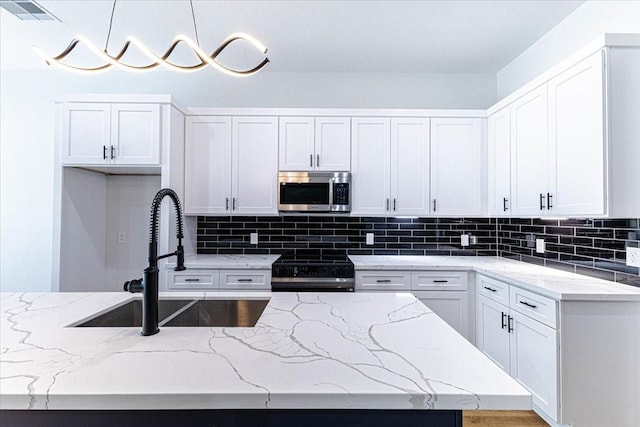 kitchen with light stone countertops, a sink, decorative backsplash, range with electric cooktop, and stainless steel microwave