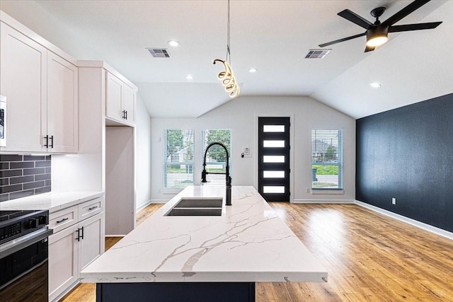 kitchen featuring electric range, an island with sink, visible vents, and a sink